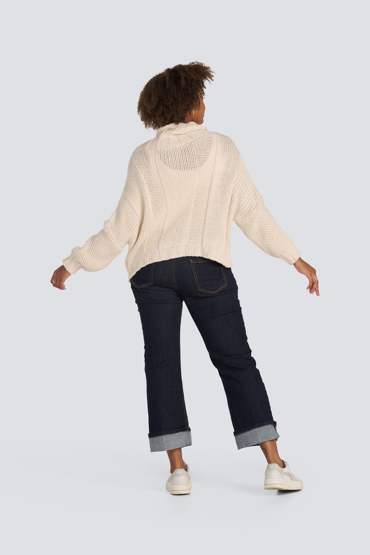 Chunky cream knit turtleneck sweater shown from behind with dark cuffed jeans.