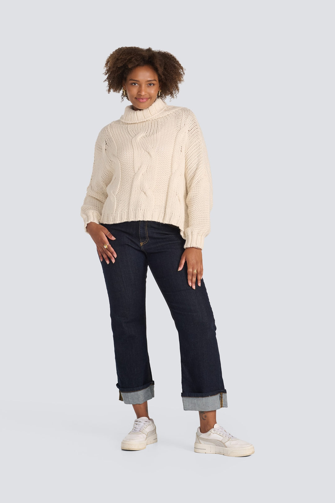 Cream cable-knit turtleneck sweater paired with dark wash cuffed straight-leg jeans.
