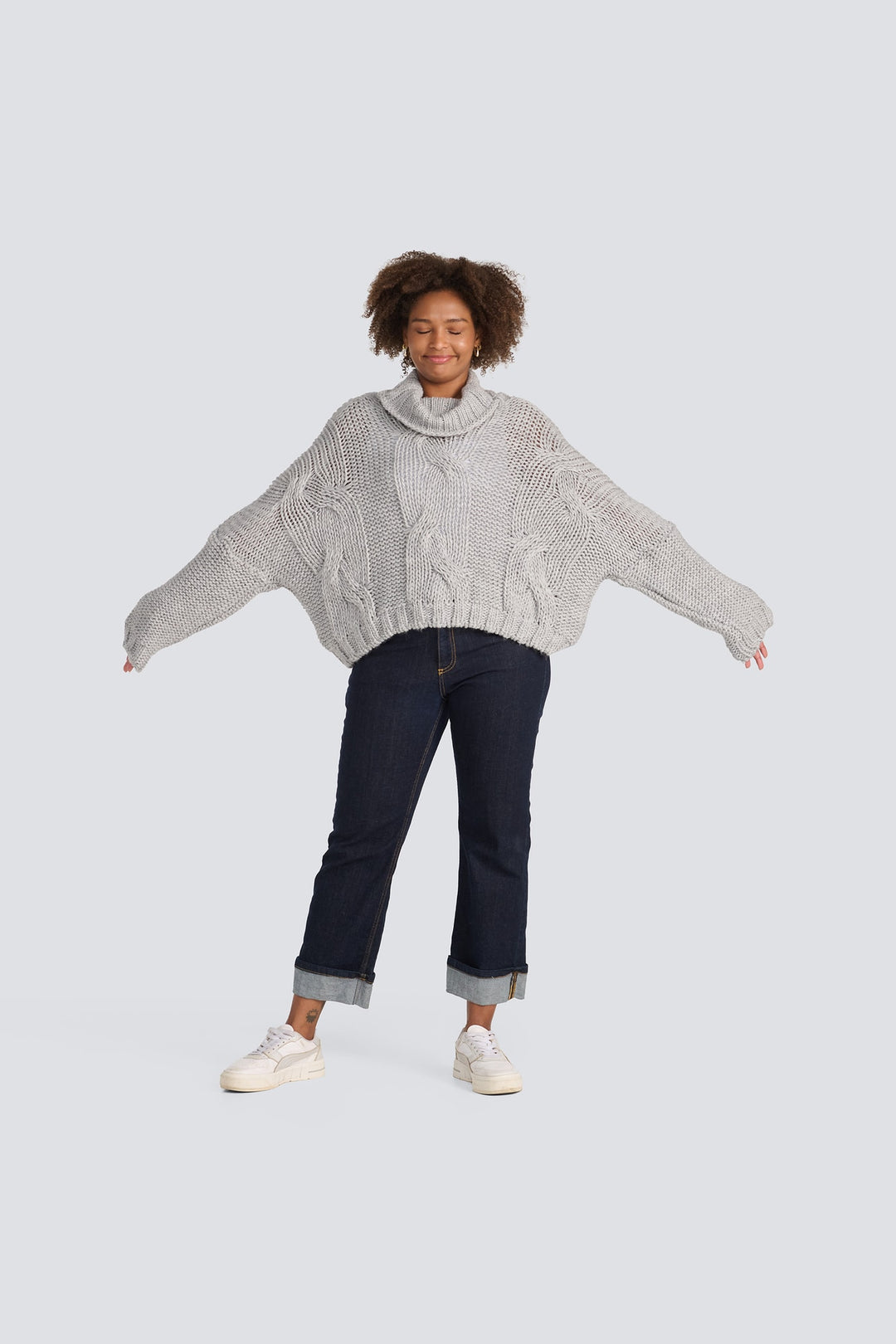 Oversized light grey chunky cable-knit sweater with a cowl neck and wide sleeves.