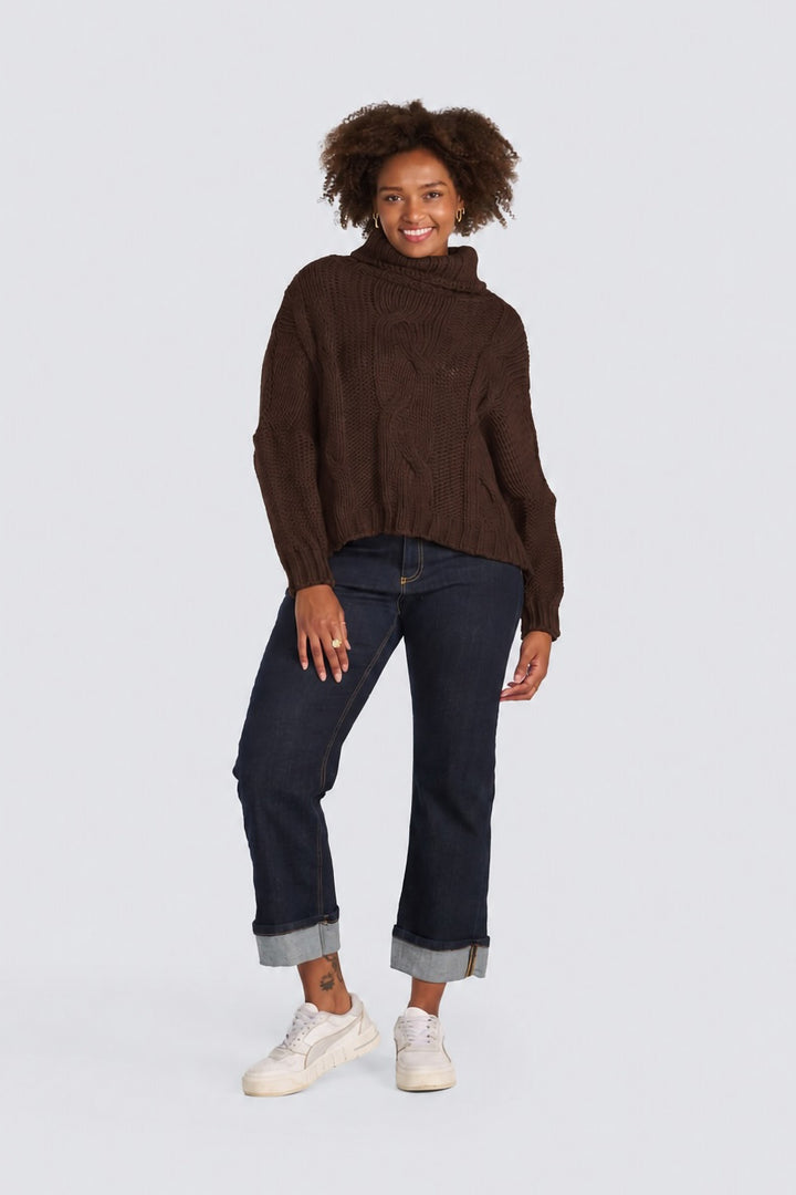 Dark brown cable-knit turtleneck sweater paired with cuffed dark-wash jeans.