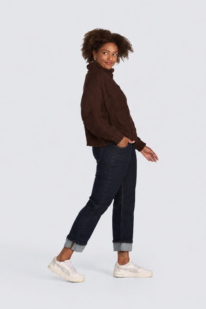 Dark brown chunky cable-knit turtleneck sweater paired with dark wash cuffed jeans.