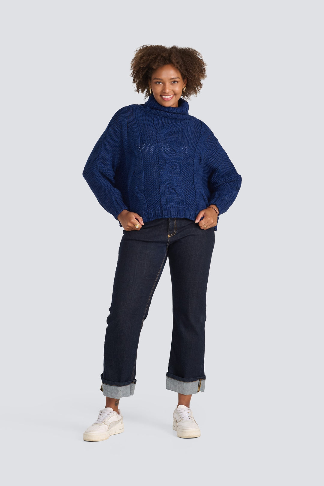 Navy blue cable-knit turtleneck sweater paired with dark wash cuffed denim jeans.