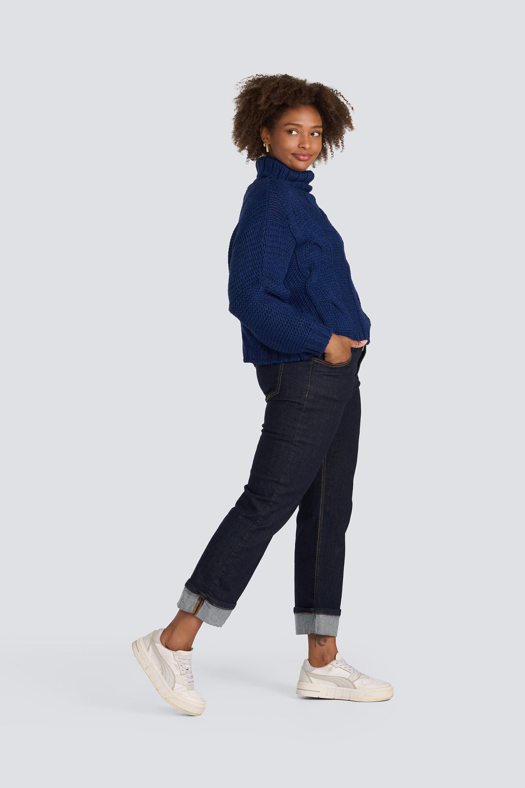 Navy blue chunky cable-knit turtleneck sweater worn with dark wash cuffed jeans.