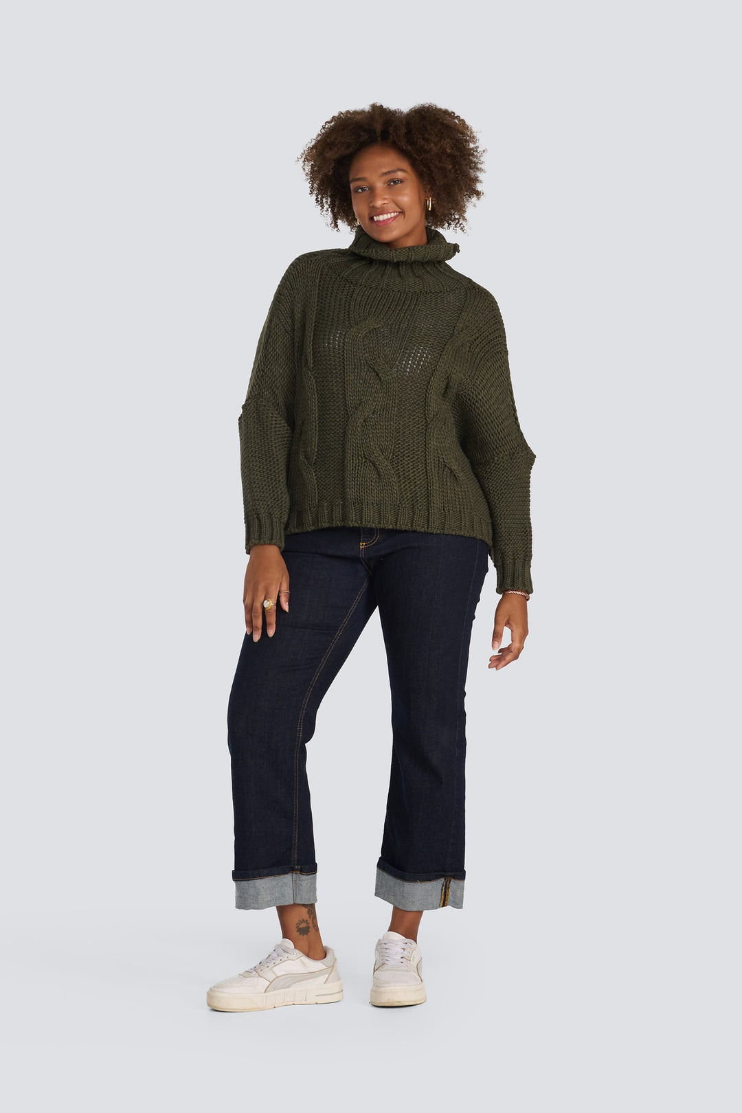 Olive green chunky cable-knit turtleneck sweater paired with cuffed dark wash jeans.