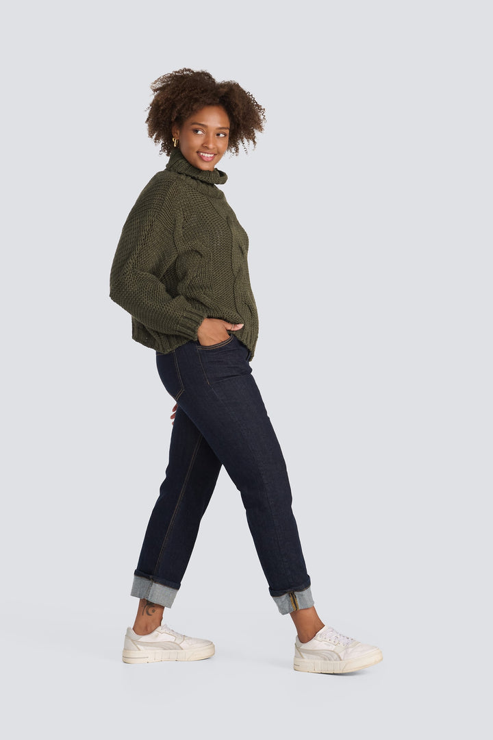 Olive green chunky cable-knit turtleneck sweater paired with dark wash cuffed jeans.