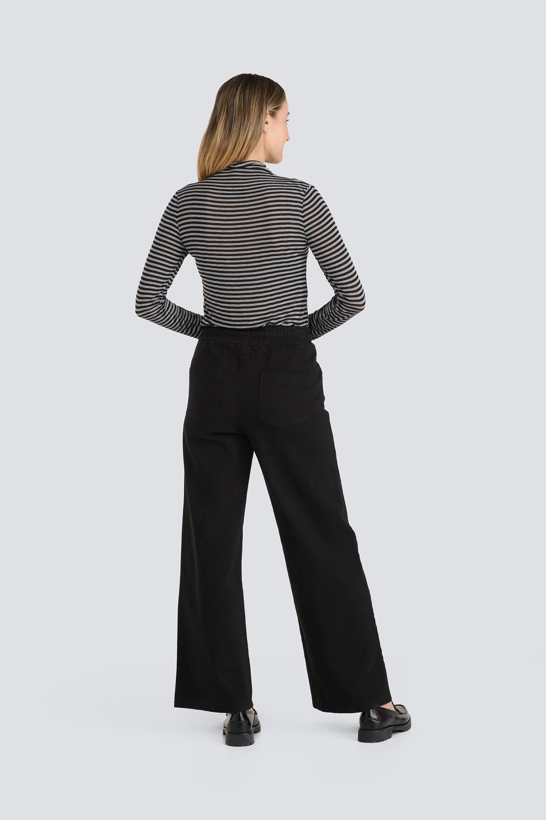 Grey and black striped long-sleeve top worn with high-waisted black wide-leg trousers.