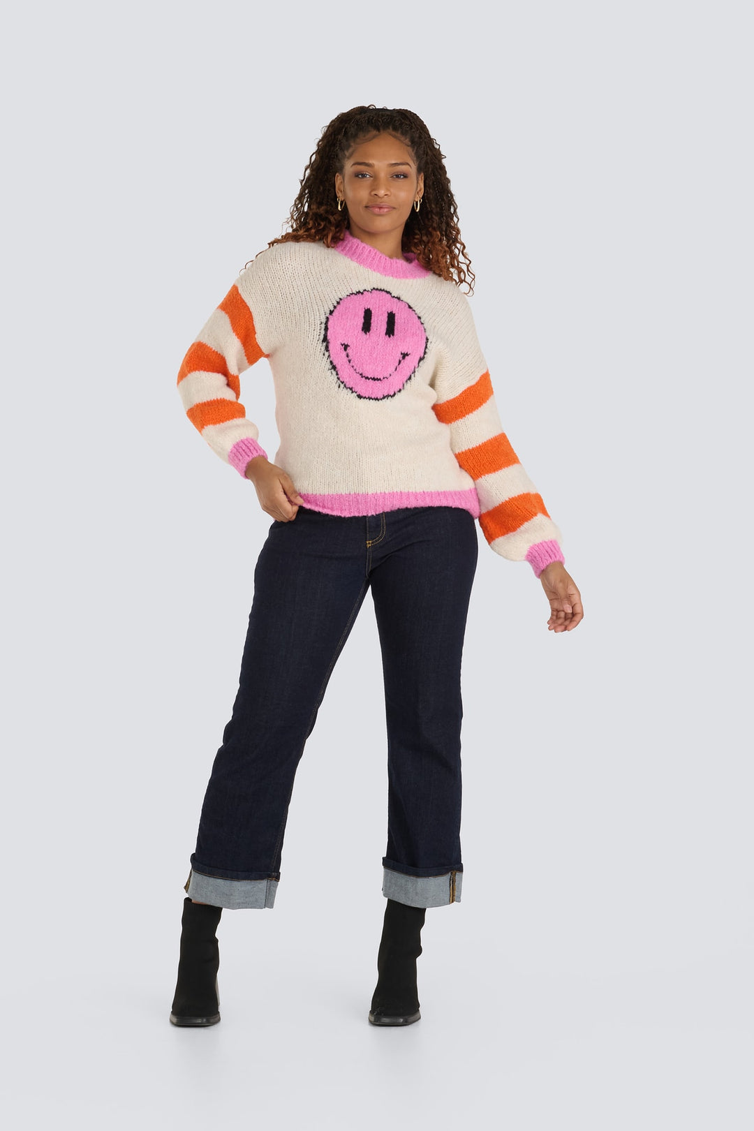 Cream knit sweater with a pink smiley face, orange striped sleeves, and pink trim.