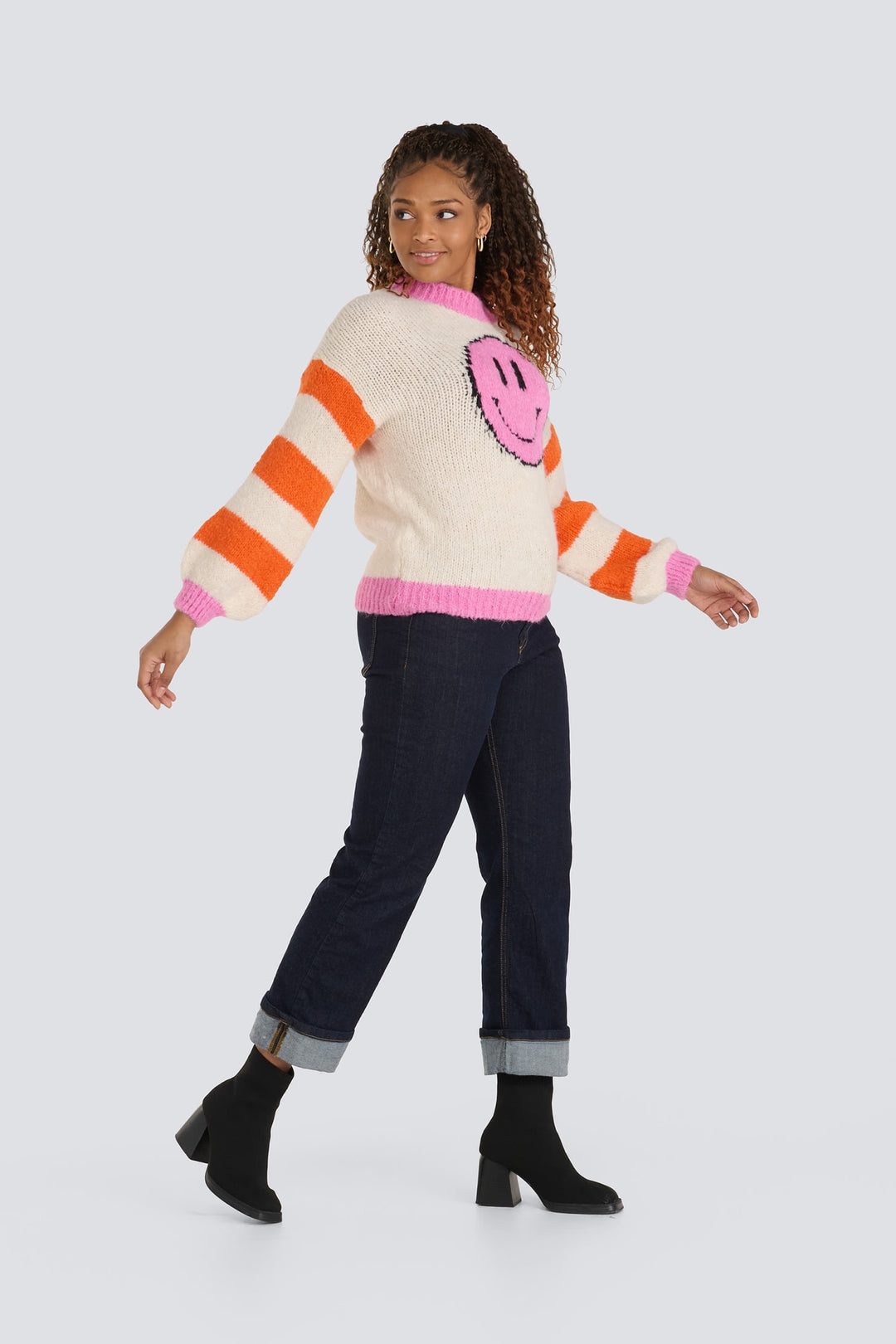 Cream knit sweater featuring a pink smiley face, orange striped sleeves, and pink trim.