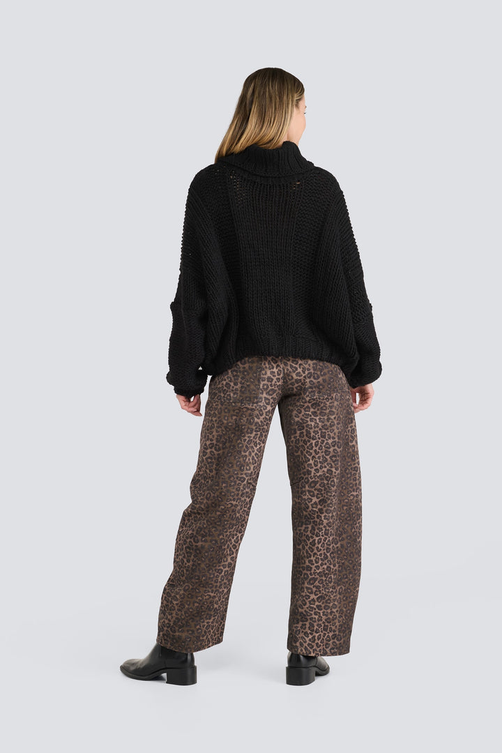 Black chunky-knit turtleneck sweater paired with brown leopard-print wide-leg pants.