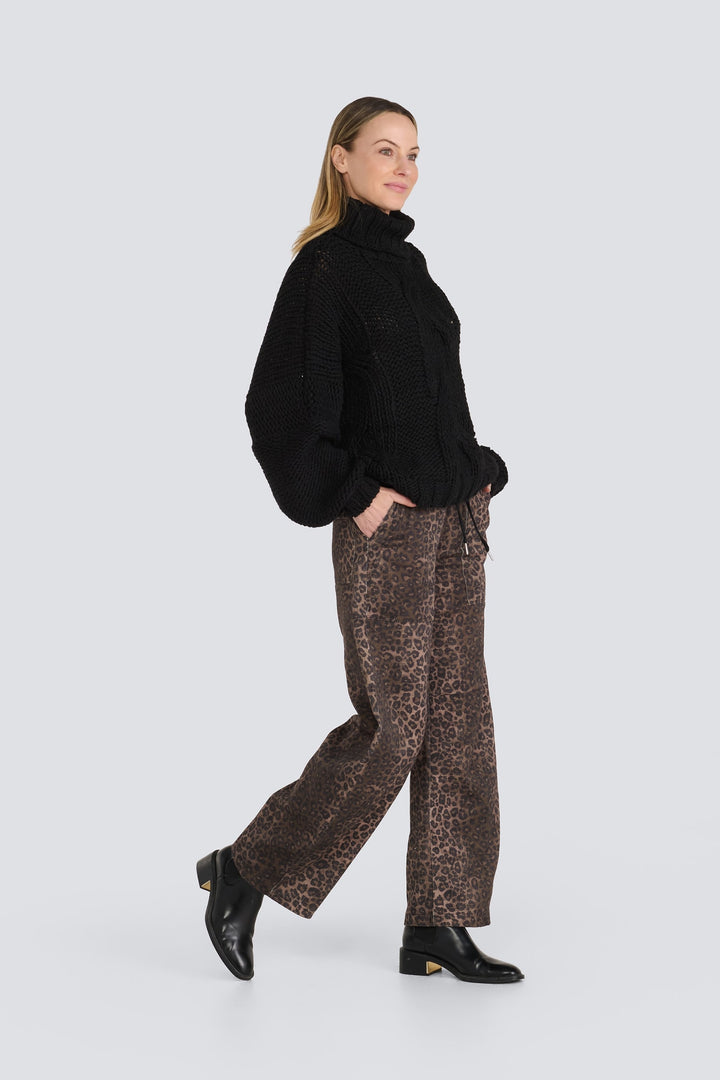 Black chunky knit turtleneck sweater paired with brown leopard print wide-leg pants.