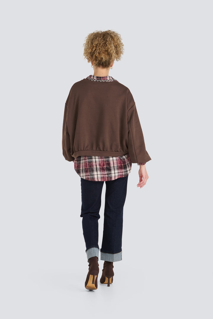 Brown loose sweatshirt layered over a burgundy plaid shirt hem.