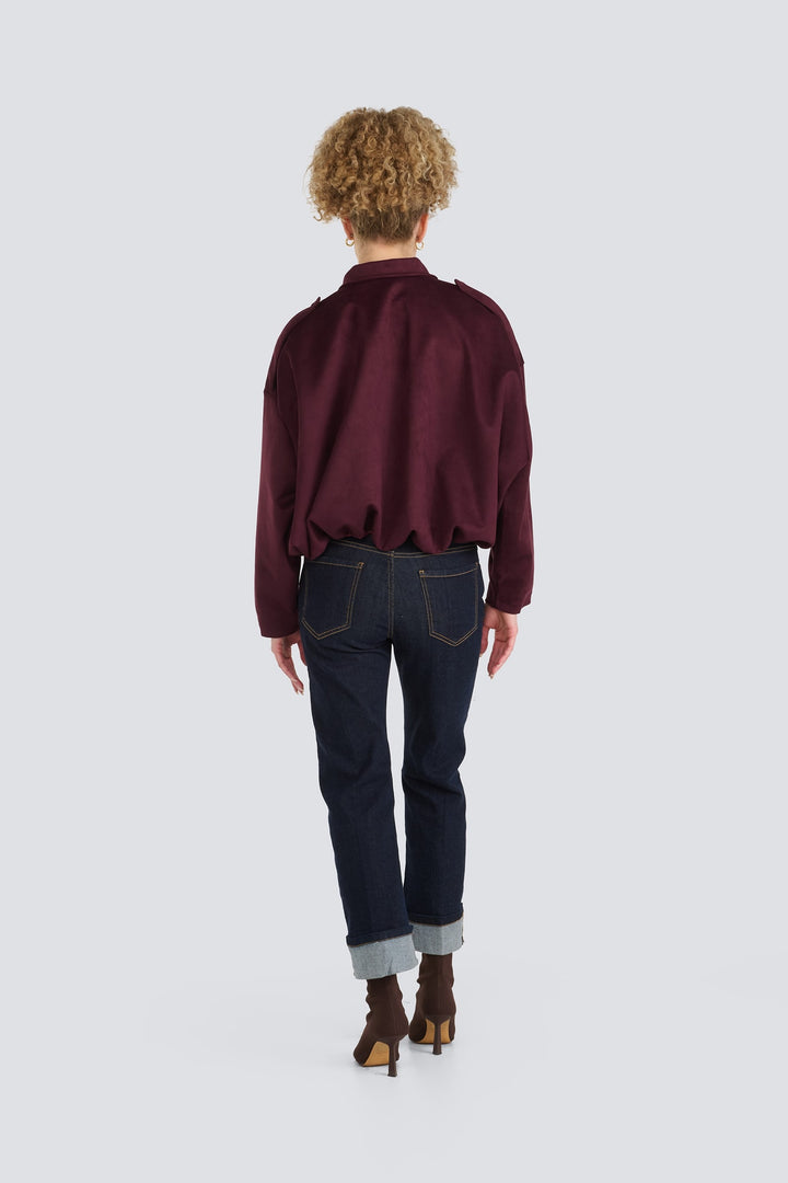 Burgundy long-sleeve jacket with a gathered hem paired with dark wash cuffed jeans.