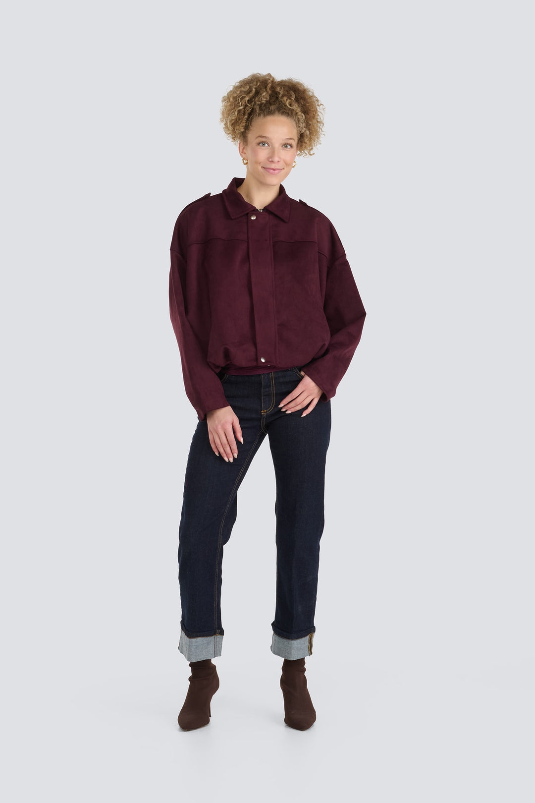 Burgundy suede jacket with snap-button closure paired with dark wash cuffed jeans.
