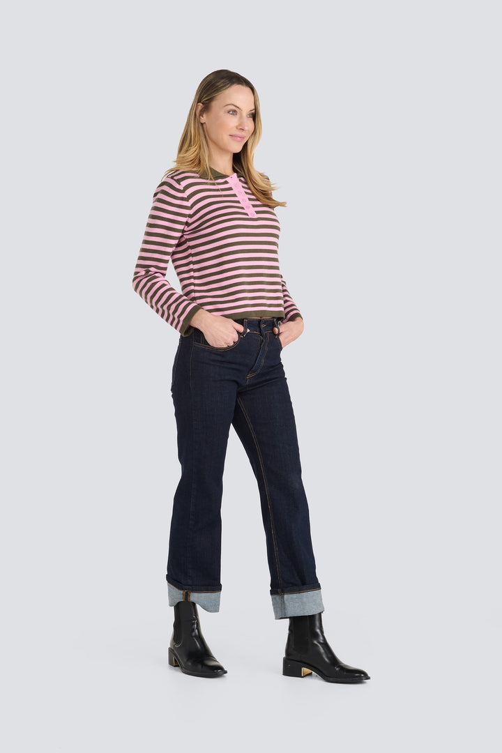 Pink and olive green striped long-sleeve henley top paired with dark cuffed jeans.